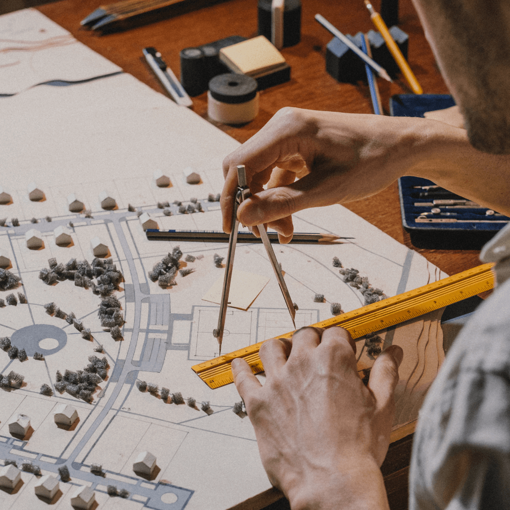 Zoom sur les mains d'un architecte tenant un compas et une règle sur un plan d'une ville